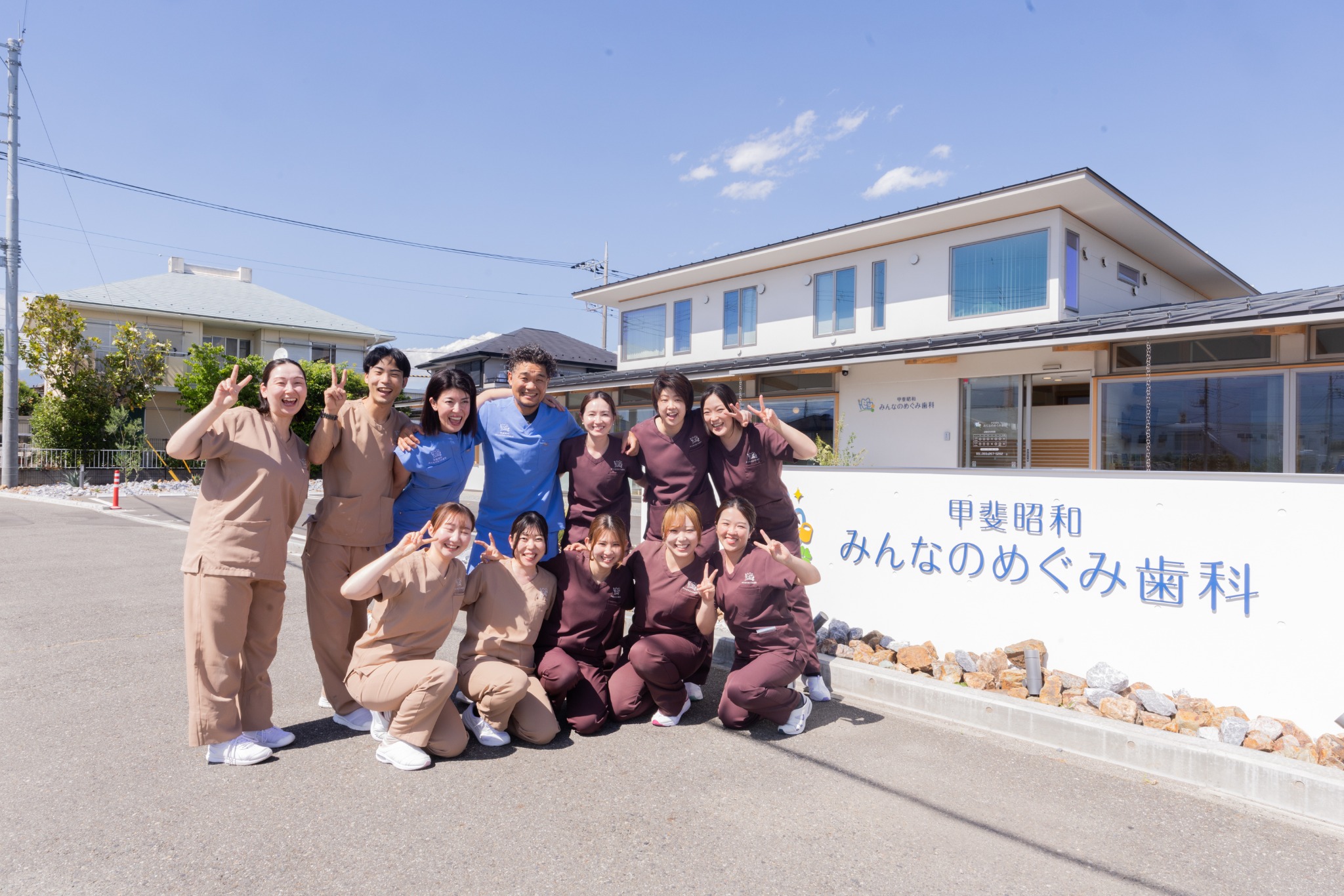 医院外観前で笑顔を見せる甲斐昭和みんなのめぐみ歯科のスタッフ集合写真